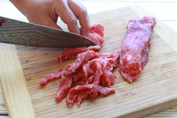 slicing flank steak on a wooden cutting board.