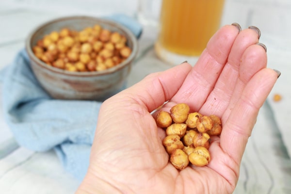 crispy spicy air fryer chickpeas in the palm of a hand and a bowl of chickpeas in the background