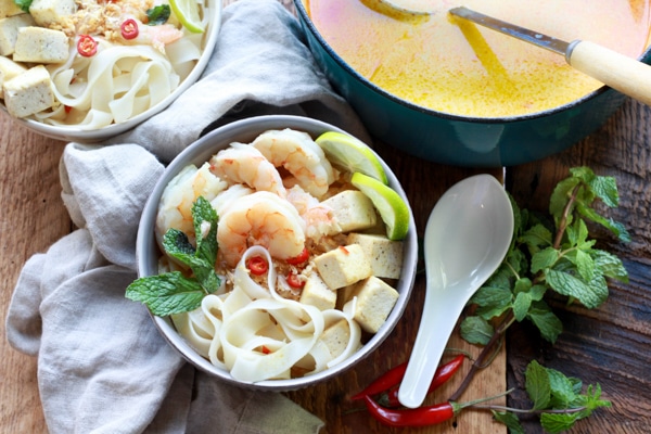 Singapore laksa with shrimp, tofu, and rice noodles in a bowl and in a Dutch oven with ladle.