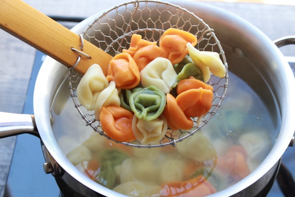 Rri-color tortellini in spider strainer being lifted out of a pot of water.