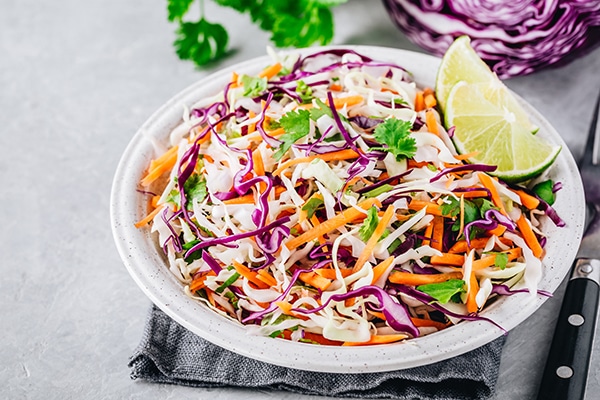 A fresh slaw in a white bowl with red and white cabbage on a gray stone background
