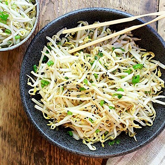 Japanese bean sprouts salad in a black bowl with chopsticks on top and a smaller bowl of bean sprouts on the side on top of a wooden board.