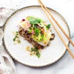 Pan seared halibut on top of a bed of quinoa and topped with a spicy nuoc cham slaw on top of a round white plate with chopsticks on the side.