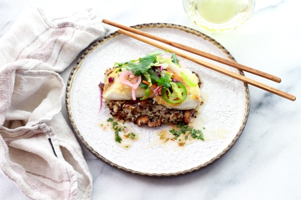 pan seared halibut on a round white plate top of a bed of quinoa and topped with a spicy nuoc cham slaw