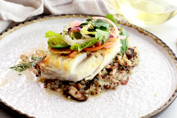 Pan seared halibut on top of a bed of quinoa and topped with a spicy Nuoc Cham slaw on a round white plate..