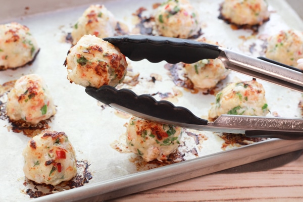 Spicy baked shrimp balls right out of the oven on a baking tray with tongs