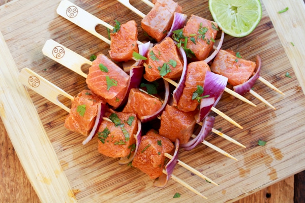 raw salmon on wooden skewers with red onion and a side of squeezed lime on top of a wooden cutting board