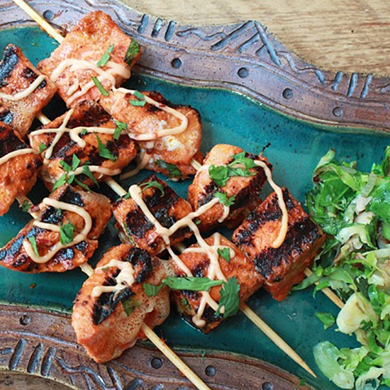 red curry salmon kebabs on skewers with a drizzle of aioli and shaved brussels sprouts on the side