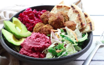 falafel balls in a bowl with beet hummus, slaw, red onions, and avocado on a white board and fork