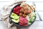 falafel balls in a bowl with beet hummus, slaw, red onions, and avocado on a white board and fork