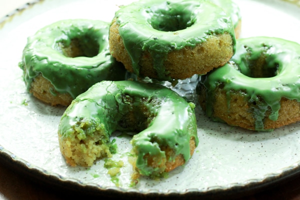 Green matcha donuts stacked on a white plate and one donut with a bite out of it