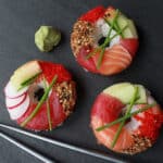 three sushi donuts on a dark gray board with silver chopsticks on the side