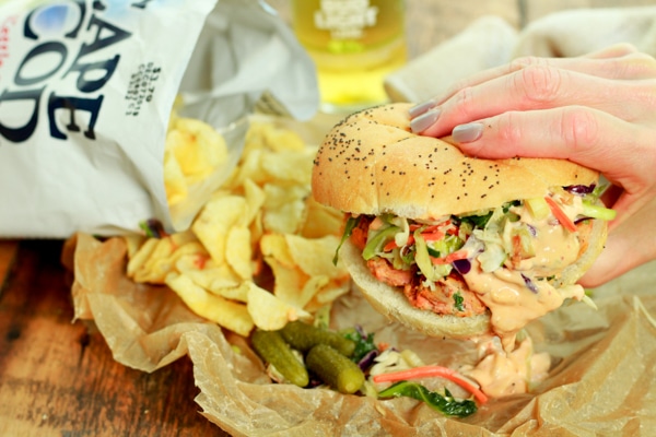 person holding a wild salmon burger over a bag of chips