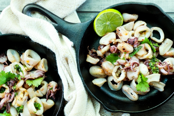 pan seared calamari in two cast iron pans with a slice of lime and a napkin on the side