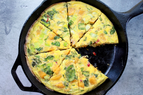 a roasted butternut squash and baby bok choy frittata in a cast iron pan on a gray board