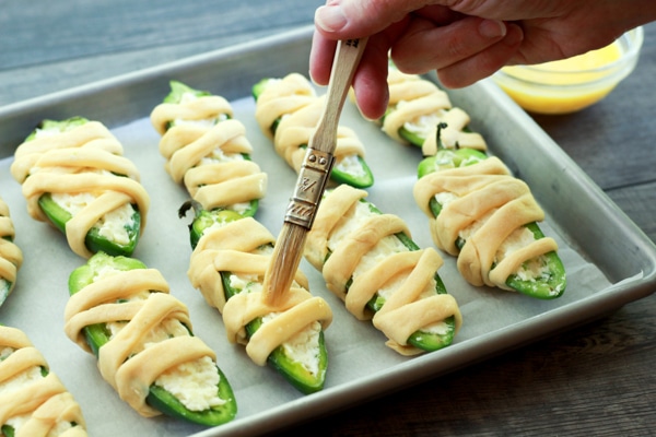 brushing and egg wash onto jalapeño poppers lined up on a baking tray with a pastry brush