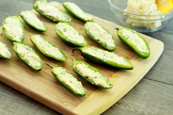 Jalapeño peppers sliced in half stuffed with cheese on a wooden cutting board