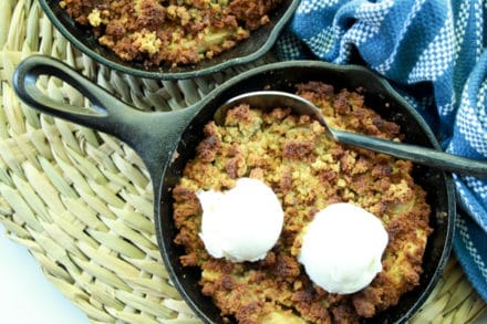 Apple crisps topped with vanilla ice cream in mini cast iron skillets with a spoon and napkin on the side