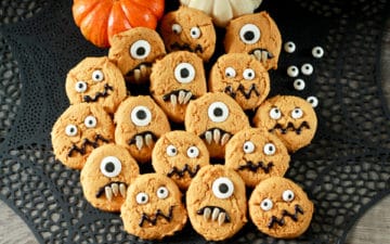 decorated pumpkin monster cookies on a black place mat with baby pumpkins on the side