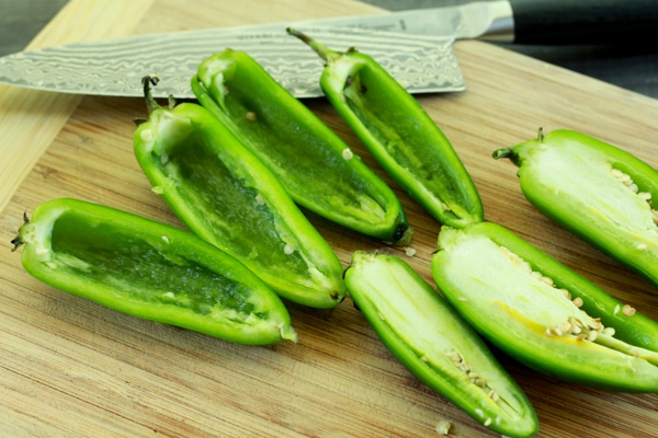 Jalapeño peppers sliced in half on a wooden cutting board and a chef's knife on the side