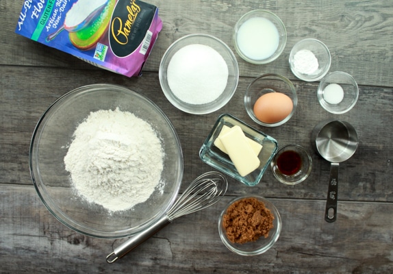 Ingredients for making gluten-free heart-shaped sugar cookies in various glass bowls on top of a wooden board.