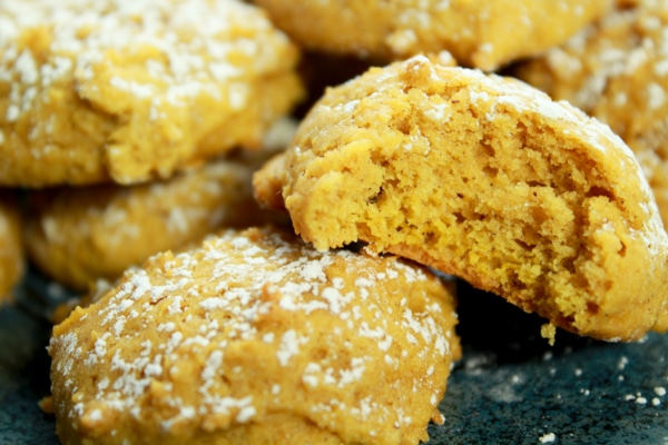 close-up shot of pumpkin spice cookies sprinkled with powdered sugar on a plate with a bite out of one cookie