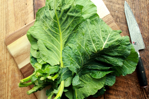 vibrant collard green leaves on a wooden cutting board with a chef's knife on the side