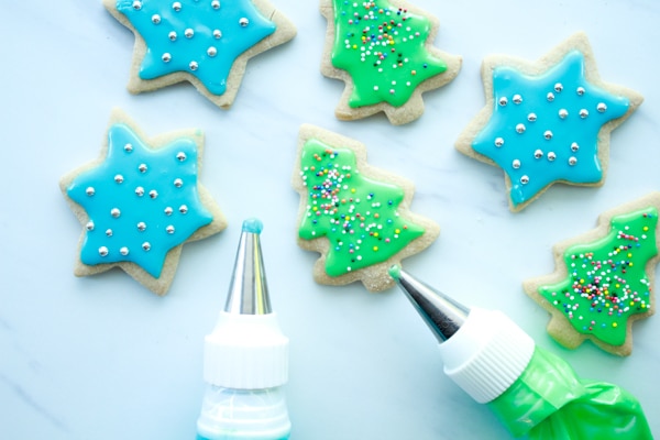 glazed and decorated blue and green gluten-free holiday cookies on a marble surface with piping bags on the side