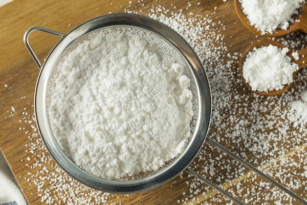 Powdered sugar in a sifter on top of a wooden board