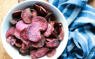 purple sweet potato chips in a white bowl with a blue napkin along side