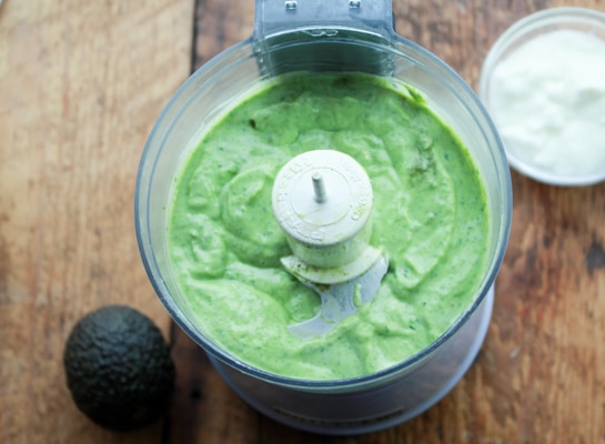 a green smoothie being blended in a food processor on top of a wooden board