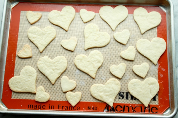 heart-shaped cookie cutouts on a baking tray lined with a silicone mat right out of the oven