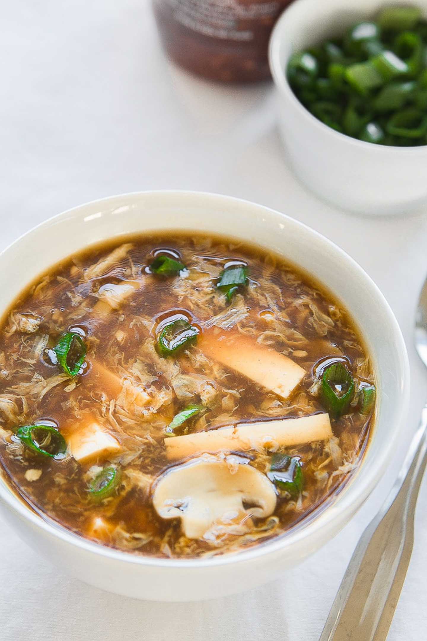 hot and sour soup in a white bowl with chopped green onions in the background