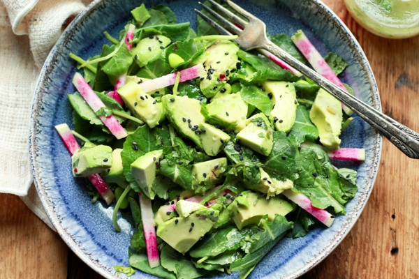 avocado-edamame kale salad in a blue bowl with a fork and dressing on the side