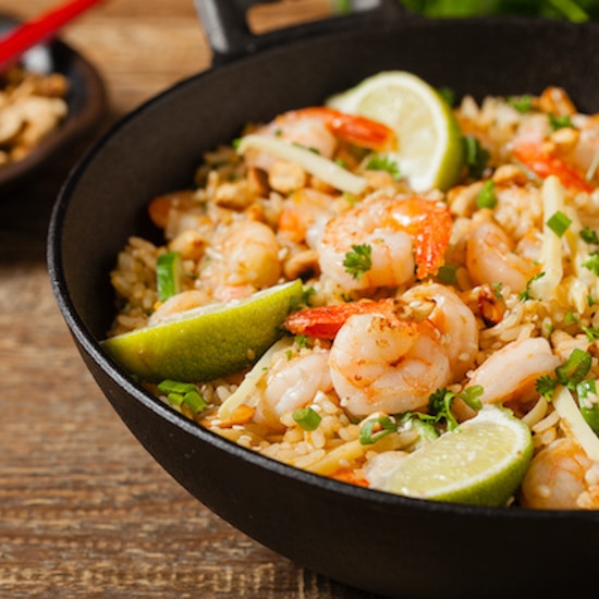 shrimp fried rice in a large black wok on a wooden board