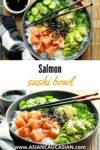 Salmon sushi bowl featuring chunks of sushi-grade salmon, sushi rice, sliced avocados, cucumbers, and seaweed strips on a bamboo mat with chopsticks.
