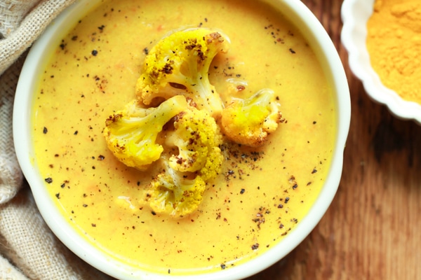 vibrant cauliflower soup in a white bowl on a wooden board