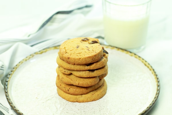 a stack of chocolate chip cookies on a white plate with a glass of milk on the side