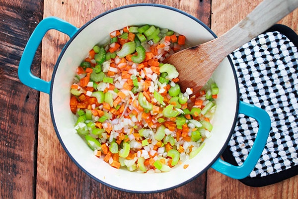 chopped carrots, celery, and onion in a soup pot on a wooden board