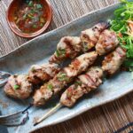 Grilled Vietnamese pork tenderloin skewers on a blue dish with a side of sauce