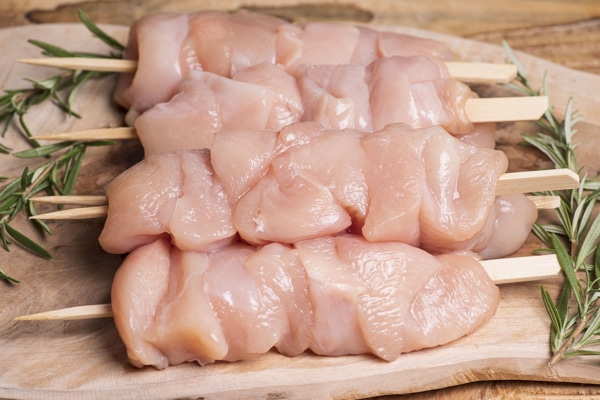 raw chicken pieces threaded onto wooden skewers on a cutting board