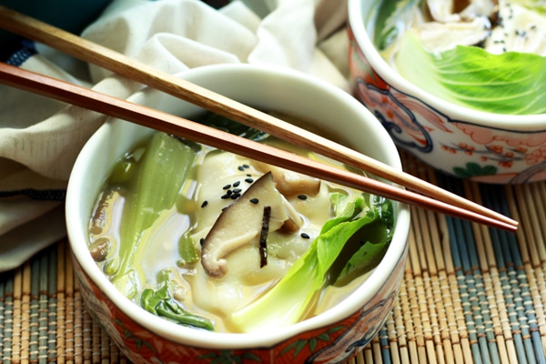 a bowl filled with vibrant wonton soup with chopsticks on a bamboo placemat