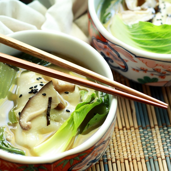 a bowl filled with vibrant wonton soup with chopsticks on a bamboo placemat