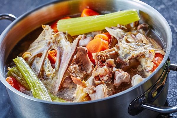 cooked turkey stock with vegetables and aromatic herbs in a stockpot, close-up, horizontal from above