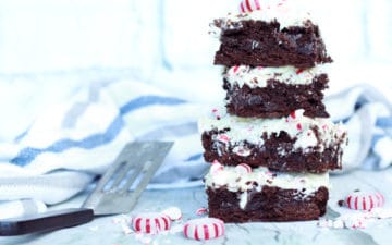 A stack of peppermint brownies on a white surface with peppermint candies along side