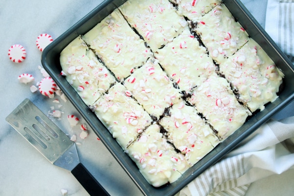 A square cake pan with cut peppermint brownies inside with pieces of peppermint candies on top