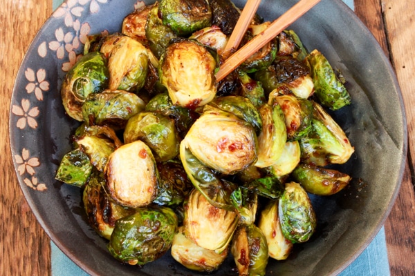 Roasted Brussels sprouts in a blue bowl with chopsticks on top of a wooden board