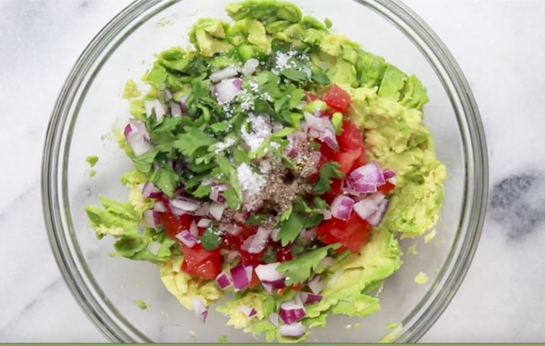 A clear glass bowl filled with ingredients for making fresh guacamole.