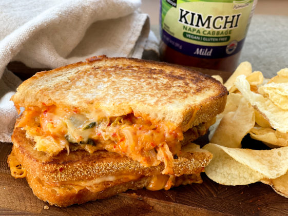 A stacked kimchi grilled cheese sandwich on a wooden board with a jar of kimchi behind it.