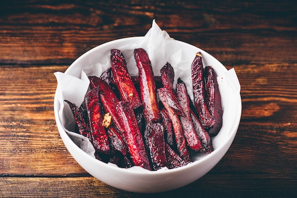 Oven baked beet fries in a white bowl on top of a wooden board.